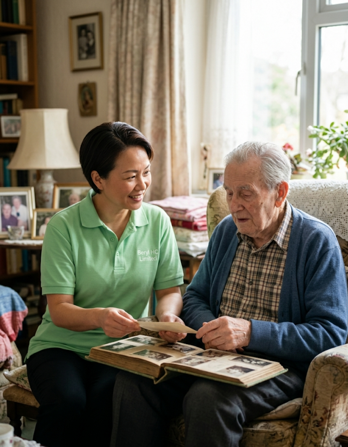 A Beryl HC Limited carer in a light green uniform sitting patiently with an elderly man with dementia, looking through a family photograph album in a calm and familiar home setting